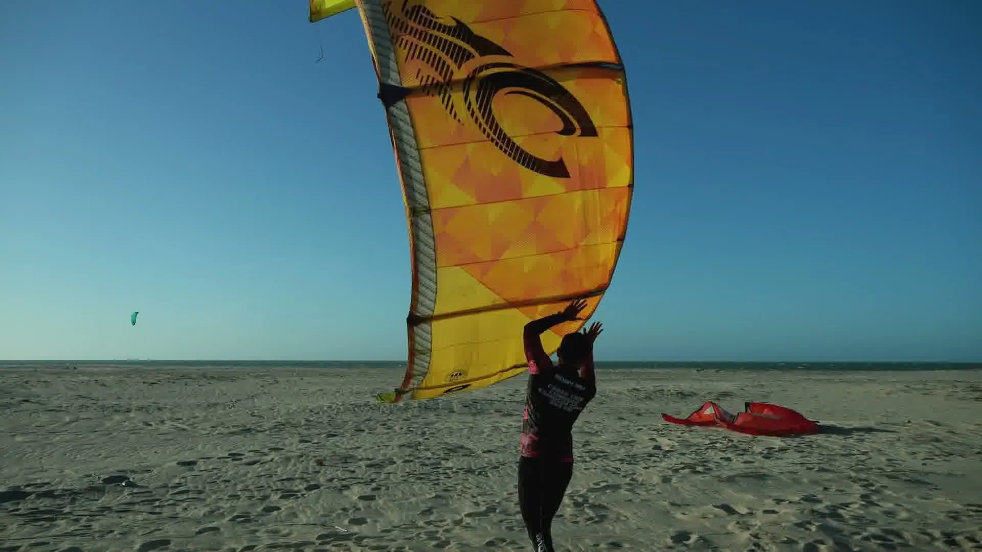 A kitesurfer readying a kite on white sand
