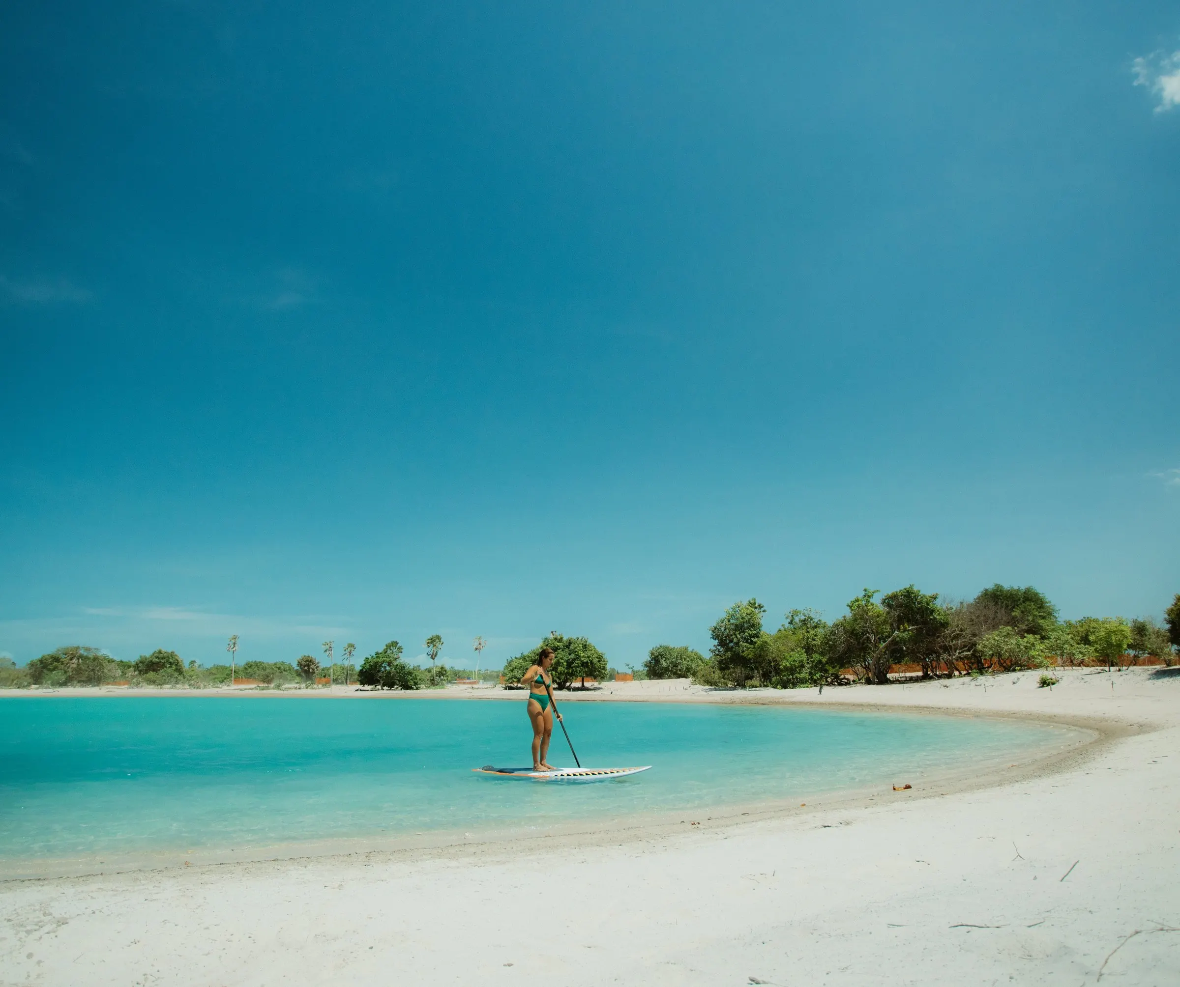 A turquoise lagoon with a paddleboarder in the distance