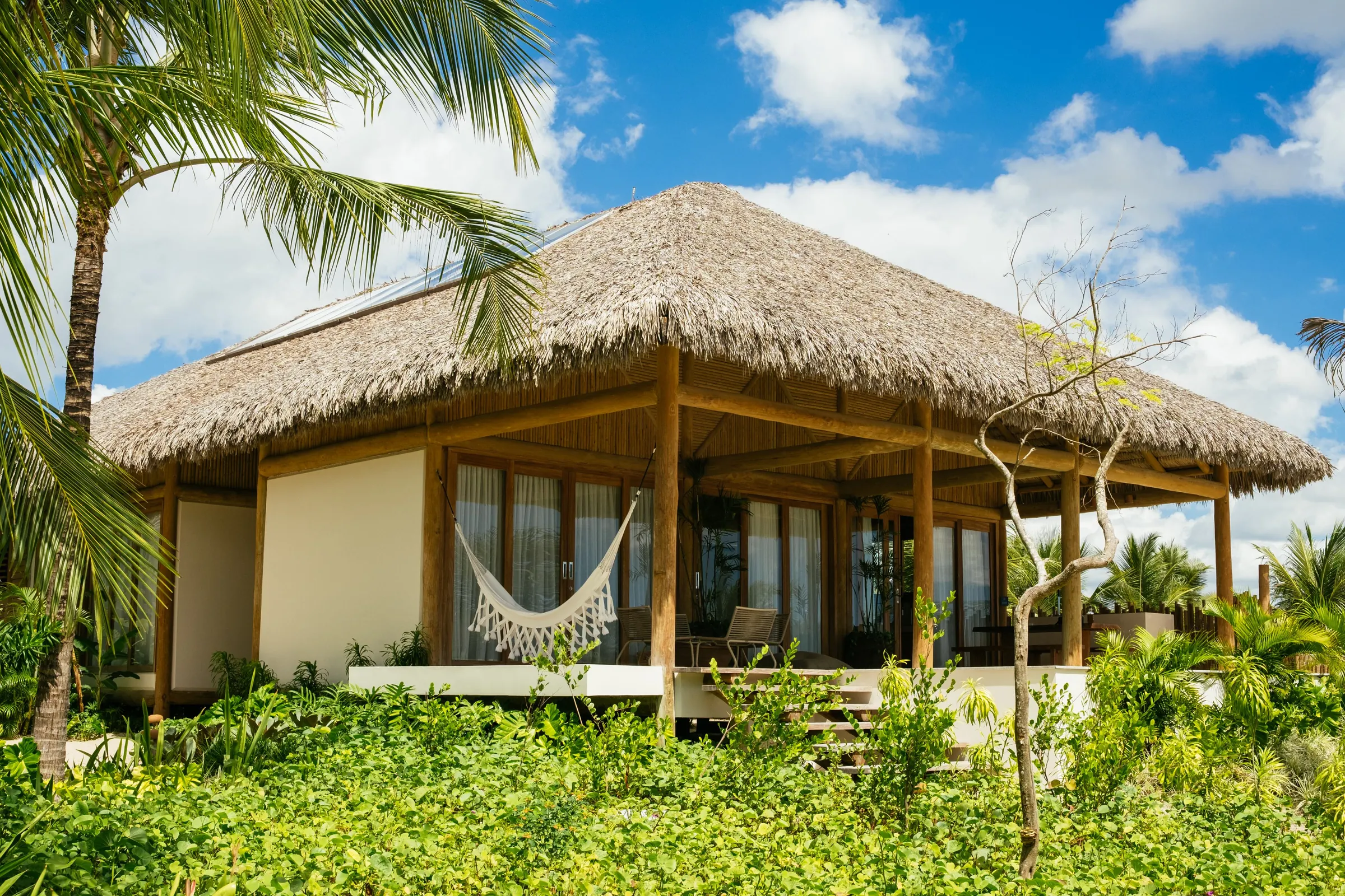 A thatched bungalow with a hammock on the veranda among palms